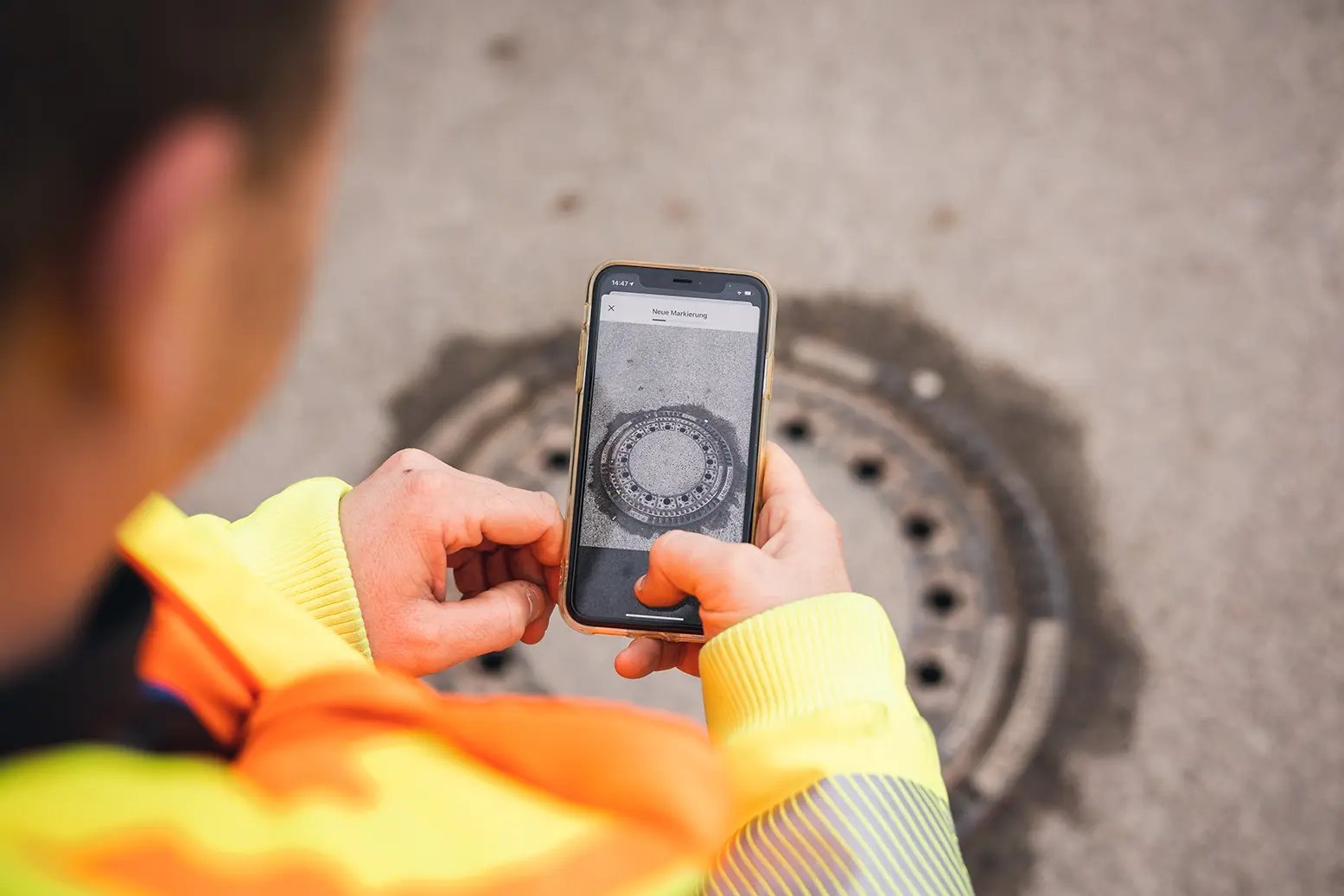 Bauhof Mitarbeiter erstellt eine neue Aufgabe von einem Schachtdeckel mit Handy in der Hand