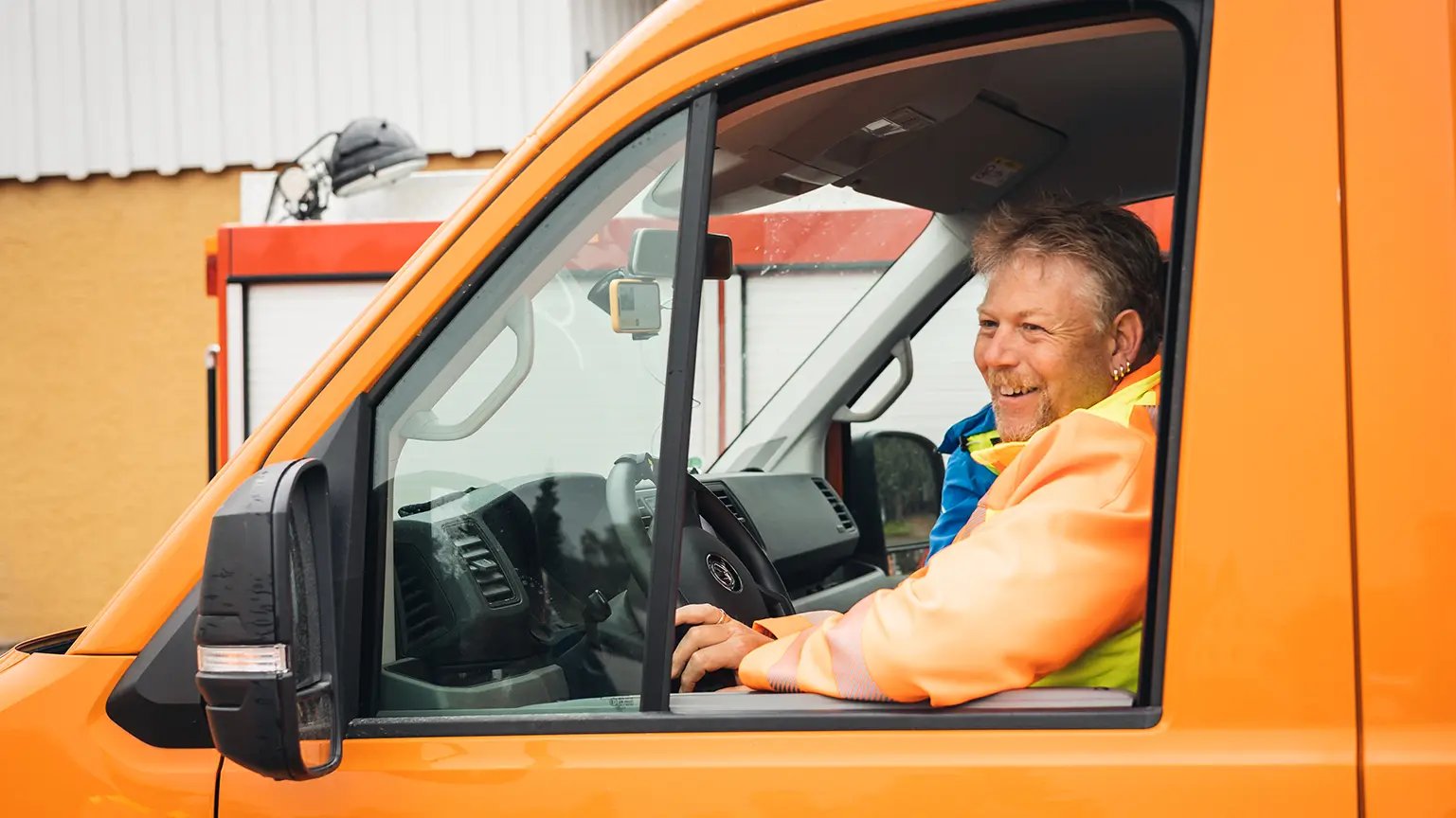 Bauhof Mitarbeiter sitzt im orangen Auto und schaut lächelnd nach draußen