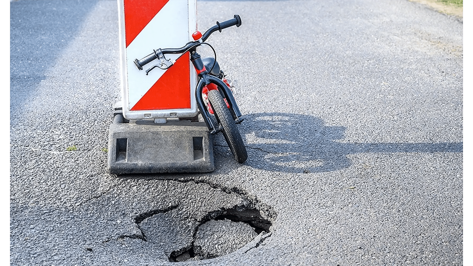 Fahrrad lehnt an einem rot-weiß gestreiften Schild vor einem Schlagloch