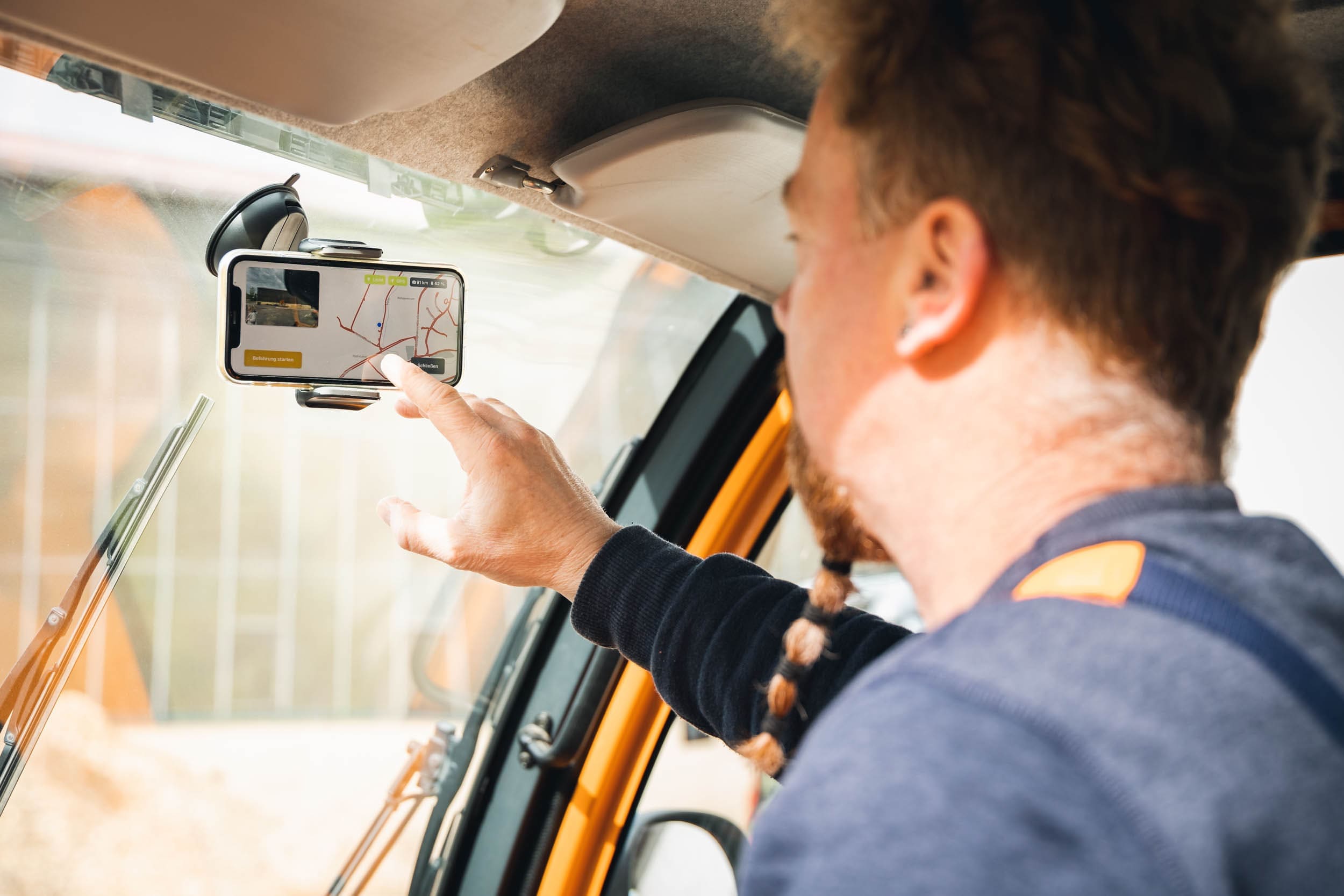 Ein Mann vom Straßenbau bedient im Auto das vialytics system auf seinem Handy welches mit einer Halterung an der Frontscheibe des Baufahrzeuges