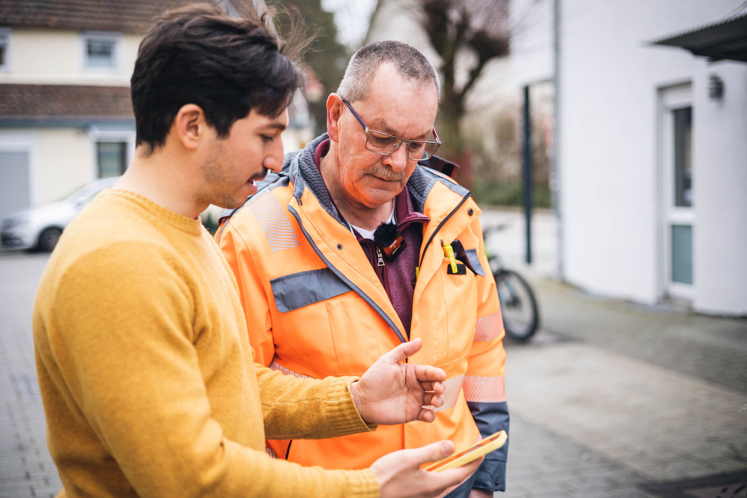 Ein Mann von vialytics zeigt einem Mann vom Straßenbau unser Straßenmanagementsystem auf dem Smartphone, draußen vor Ort auf der Straße