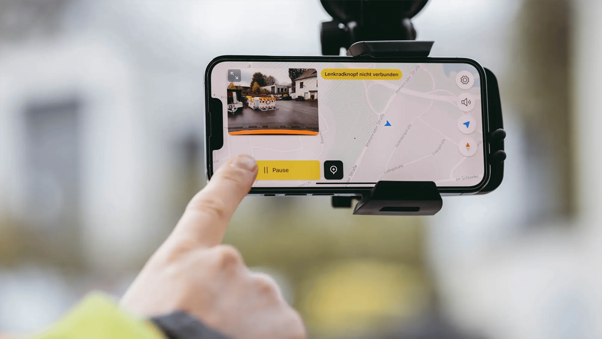 Eine Person zeigt mit dem Zeigefinger auf ein iPhone in einer passenden Halterung an der Windschutzscheibe im Auto. Auf dem iPhone ist die vialytics App aktiv.