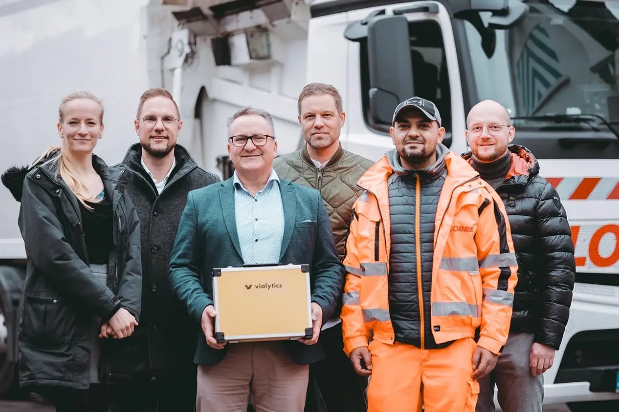 6 Personen stehen vor einem Fahrzeug in Menden. Eine Person hält einen vialytics-Koffer in den Händen. Alle sehen positiv gestimmt aus.
