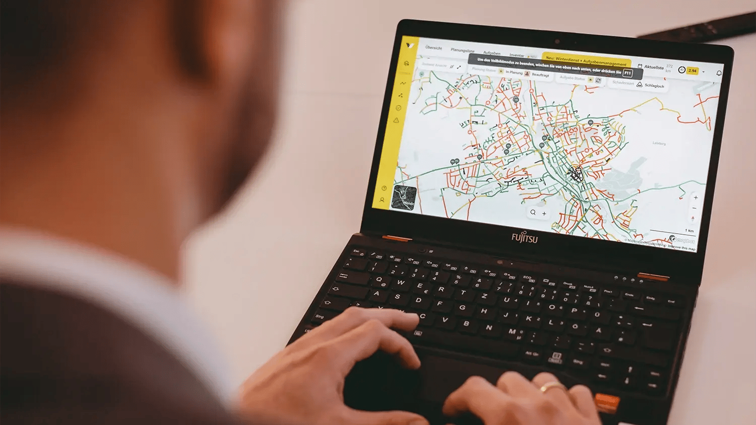 Eine männliche Person betrachtet das Web-System von vialytics auf seinem Laptop. Eine Kartenansicht des vialytics Systems ist auf dem Monitor zu sehen.