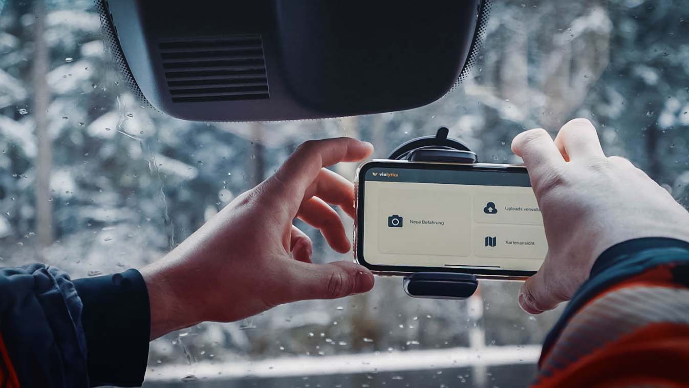 In einem Auto wird ein Handy in eine Halterung an der Windschutzscheibe angebracht. Auf dem Display ist das vialytics System für die Zustandserfassung zu sehen