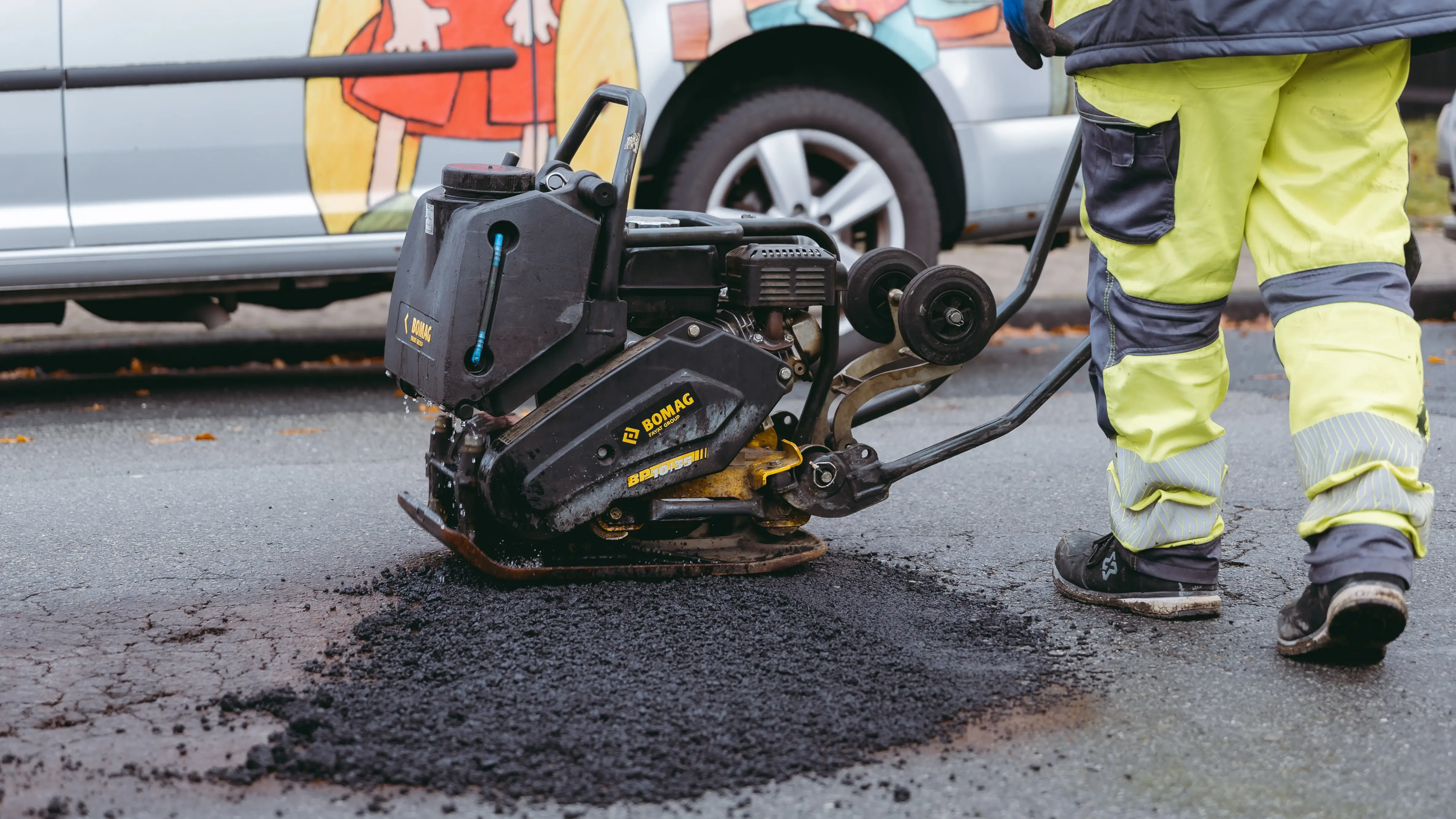 Ein Straßenschaden einer Straße wird von einem Mitarbeiter mit einer Maschine ausgebessert.